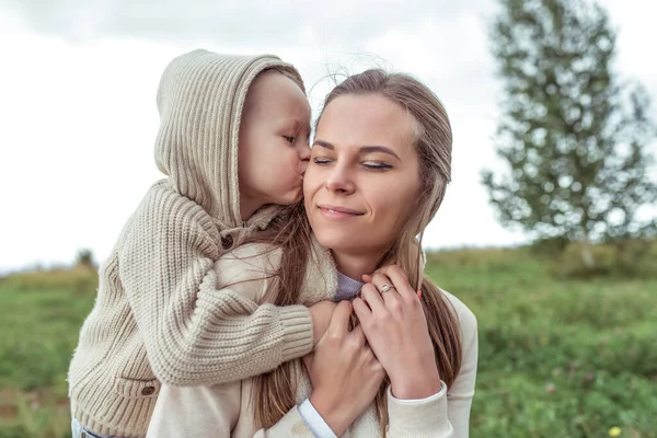 Keluarga muda, ibu wanita, memeluk anak, anak kecil, anak mencium orang tua, taman musim gugur. Emosi kenyamanan, senyuman kenikmatan. Cinta keibuan. Baju kasual. Merawat anak dan pengasuhan. — Stok Foto