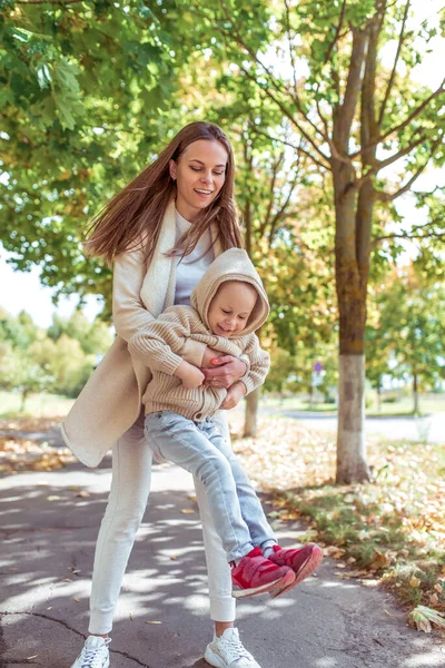 Kadın anne 3-5 yaşlarında bir çocukla oynuyor. Autumn Park şehri. Arka plandaki ağaçlar çimlerin üzerinde yaprak bırakıyor. Sıcak tutacak elbiseler. Şehirde yürü. Ebeveyn bakımı. Duygular mutluluk neşe kahkaha. — Stok fotoğraf
