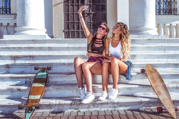 Zwei Mädchen Freundinnen schön modisch, Fotografieren Telefon, Selfie, Videoanruf Smartphone, glücklich lächelnd, Ruhe Aufnahme Videobotschaft. soziale Netzwerk App Internet. Longboard-Sommerstadt. — Stockfoto