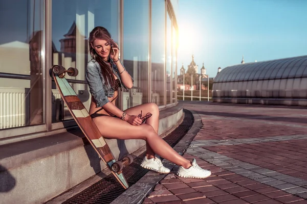 A beautiful and happy girl calls on a smartphone, smiles, rejoices and laughs. Free space for copy text. Sits in a hand sunglasses. Tanned and slender figure of a woman. — Stock Photo, Image