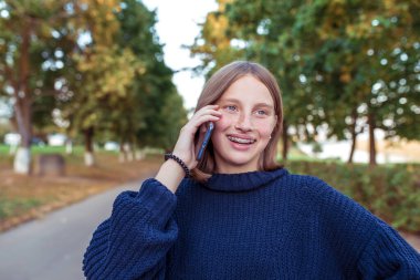 Parantez içinde mutlu bir kız, gülümseyen sevinçler, telefonla genç aramaları, akıllı telefon eli, sesli mesajları dinleyen, internetteki. Yaz parkında. Hafta sonu dinlen. Duygular mutluluk, neşe neşe kahkaha.