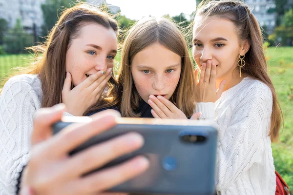 3 teenage girls watching video on phone. In summer in city. Emotions of surprise, surprise, delight, fear. Selfie photo. Video recording. Social networks, video clip on Internet. Online application.