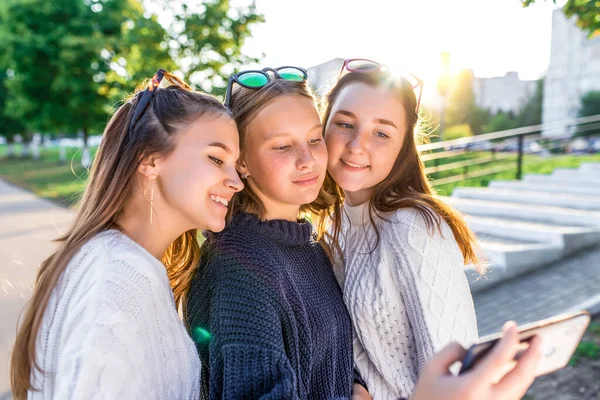 3 девочки-подростка 12 13 14 лет, летний парк, держащие в руках смартфон, фото селфи. Праздничные выходные, лучшие друзья, эмоции счастья, веселая улыбка. Социальные сети в Интернете, онлайн-приложение . — стоковое фото