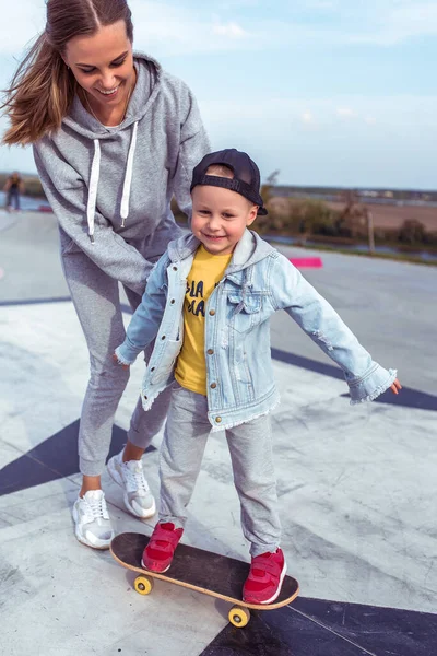 Keluarga bahagia, ibu wanita, anak skate di skateboard, membantu dukungan dalam pelatihan dalam kebugaran olahraga. Emosi kebahagiaan menyenangkan relaksasi dan sukacita, senyum dan tawa. Lapangan olahraga musim panas . — Stok Foto