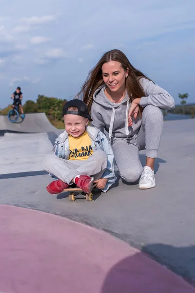 Keluarga bahagia, ibu wanita, skate anak skateboard, membantu dukungan dalam pelatihan dalam kebugaran olahraga. Emosi kebahagiaan, kesenangan relaksasi dan sukacita, senyum dan tawa. Lapangan olahraga musim panas . — Stok Foto