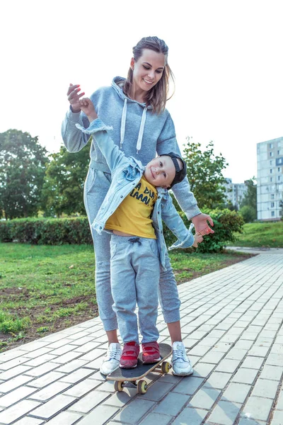 Young family, mother woman little boy 3-5 years son, summer city. Skateboarding education, balance training help support of parent raising child. Emotions positive happiness joys, fun smile laughter. — Stock Photo, Image