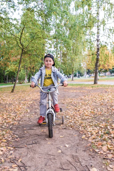 Anak kecil berusia 3-5 tahun, taman musim panas, pohon latar belakang. Kereta belajar menjaga keseimbangan sepeda, naik pedal. Di musim panas di kota, emosi kenyamanan kebahagiaan. Pakaian santai, topi baseball denim . — Stok Foto