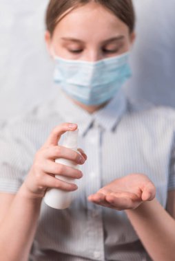 11-14 yaşlarındaki genç kız, tıbbi maske takıyor, elinde antiseptik sprey tutuyor, bakterilerin ellerini dezenfekte ediyor, COVID-19 salgın hastalık salgını koruma konsepti.