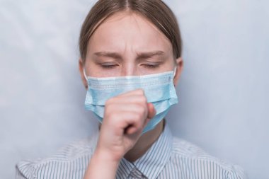 12-15 yaşlarında, tıbbi maskeli genç bir kız, yüzünü kapatıyor, gözleri kapalı, kendini kötü hissediyor ve öksürüyor. Beyaz arka plan, elleri ağzını kapatıyor, COVID-19 salgın hastalık belirtileri.