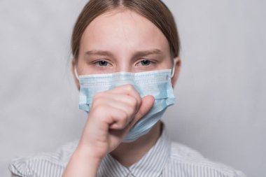 Genç kız 11-15 yaşlarında, tıbbi maske takıyor, ağzını eliyle kapatıyor, boğazı ağrıyor, öksürüyor. Beyaz arka plan, risk kirliliği diğerleri, COVID-19 salgın hastalık belirtileri konsepti