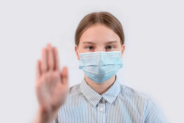 Teenager κορίτσι 12-15 ετών, σε μια ιατρική μάσκα καλύπτει το πρόσωπό της, stop hand χειρονομία, προσοχή είναι επικίνδυνη, λευκό φόντο, COVID-19 sars-cov-2 επιδημία πανδημία ιού επιδημία έννοια προστασίας. — Φωτογραφία Αρχείου