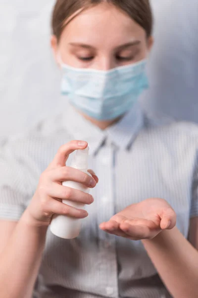Teenager girl of 11-14 years old, in medical mask covers face, holds an antiseptic spray in hand, disinfects hands from viruses bacteria, COVID-19 epidemic pandemic virus outbreak protection concept. — Stock Photo, Image