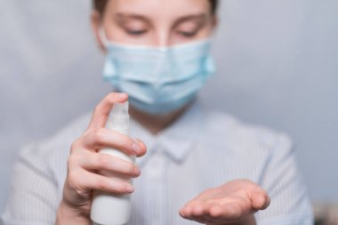 Yakın plan, genç kız, çocuk elleri, elinin antiseptik avuçlarını, dezenfeksiyon emniyetini, grip salgınını ve salgın hastalıkları önlemeyi uygular. Beyaz arka planda tıbbi maskeyle.
