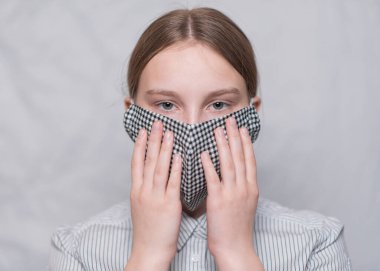 Yakın plan portre, 15 yaşında genç bir kız, maske takıyor, avuçlarıyla maske takıyor, grip salgını ve salgın hastalıklarını önlüyor. Beyaz arka planda tıbbi maskeyle.
