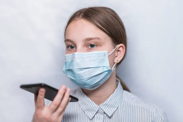 Teenager girl of 12-15 years old, protective medical mask, records voice message smartphone, online application, talking remotely with parents, communication Internet. Pandemie chřipkové infekce. — Stock fotografie