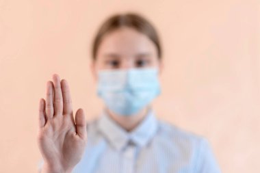 Bej arka plan, yakın plan elde odaklanma, tıbbi lekelenmiş genç kız yüzünü kapatıyor, kameraya bakıyor. Corona virüsünün salgınını yavaşlatmaya yardım et, evde kal, mesafeyi koru ve hijyenik kavramsal poster