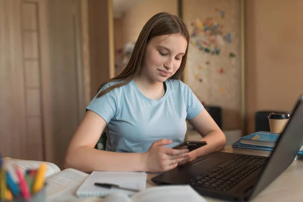 Nastolatka szczęśliwa uśmiecha się, odrabia lekcje na laptopie internetowym, smartfonie, połączeniach społecznych 4G 5G. Szkolenie na odległość podczas kwarantanny. Kontekst książki wykłady na temat instytutu szkolnego — Zdjęcie stockowe