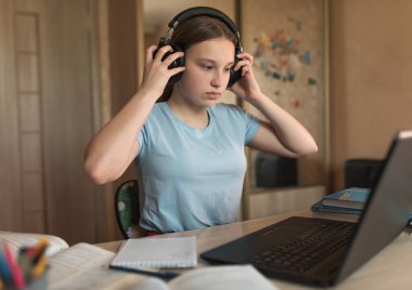 12-14 yaşlarında genç bir kız, kulaklık takıyor, dizüstü bilgisayar dersleri alıyor, video izliyor, müzik dinliyor. E-eğitim mesafesi internet video iletişimi öğreniyor. Film öğretim videoları izle.