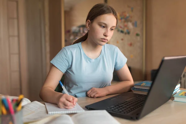 Концентрированная девочка-подросток 12-14 лет, домашний, ноутбук уроки, ноутбук пишет ручку. Электронное образование дистанционное обучение Интернет и видеосвязи. Проведение уроков и экзамен . — стоковое фото