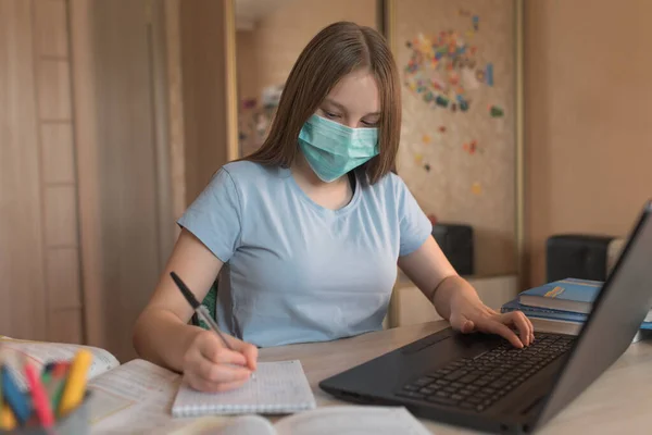 Teenager dívka 12-15 let, lékařská maska, psaní doma, lekce laptopu. E-vzdělávání distanční vzdělávání Internet a video komunikace. Ochrana proti bakteriím a kovirům, zůstaňte doma. — Stock fotografie