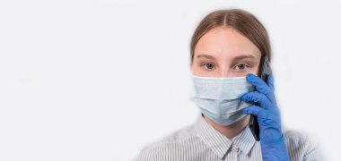 Genç kız, beyaz arka planda tıbbi maske takıyor, gözlere odaklanıyor, akıllı telefona odaklanıyor, ücretsiz uzay fotokopisi mesajı yazıyor, virüs virüsü hastalığı, evde kalıp, salgın koronovirüs kovirüsü 19 'u durduruyor.,