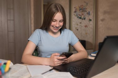 Genç kız, mutlu gülümseme, sınavı geçme, piyango kazanma, şans başarısı, akıllı telefon elinde, evde elektronik eğitim dizüstü bilgisayarı internette video izliyor. Üniversite için okul eğitimi hazırlığı.