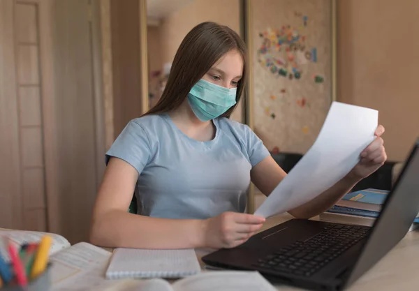 Menina adolescente em máscara médica protetora, em mãos carta de folheto de admissão de teste, infecções virais de segurança, educação eletrônica em casa, laptop e notas. Educação escolar, faculdade de preparação . — Fotografia de Stock