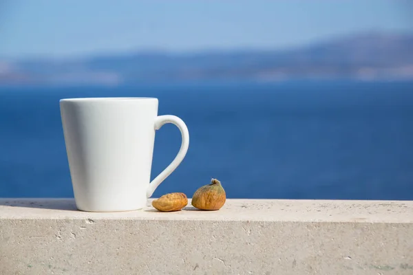 Witte cup met koffie en twee vijgen op een achtergrond van blauwe zee en de bergen — Stockfoto