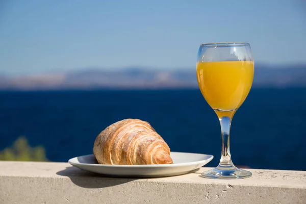 Croissant a sklenice pomerančové šťávy na pozadí moře v Chorvatsku — Stock fotografie