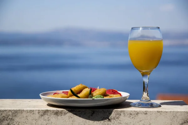 Gebakken calamares met tomaat Salade en sinaasappelsap in een glas op een achtergrond van de zee — Stockfoto