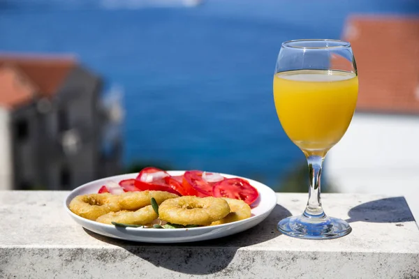 Gebakken calamares met tomaat Salade en sinaasappelsap in een glas op een achtergrond van de zee — Stockfoto