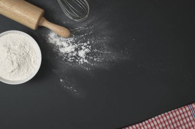 Tahta hamur silindiri, bir bardak un ve un serpiştirilmiş siyah masaya çırpma. Pastane ev yapımı konsept.