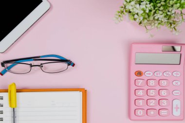 Pastel pembe ofis masasında defter, tablet, gözlük ve hesap makinesi var. Kopyalama alanı olan üst görünüm. Çalışma masası konsepti.