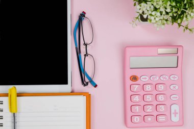 Pastel pembe ofis masasında defter, tablet, gözlük ve hesap makinesi var. Kopyalama alanı olan üst görünüm. Çalışma masası konsepti.