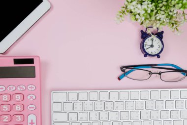Pastel pembe ofis masasında defter, saat, tablet, gözlük ve hesap makinesi var. Kopyalama alanı olan üst görünüm. Çalışma masası konsepti.