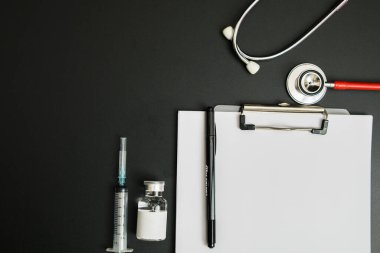 Doctor 's Day ve Covid-19 konsepti. Klip tahtasında beyaz ilaç şişesi, iğne ve steteskop var.