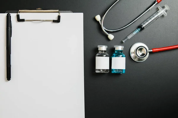 Doctor 's Day ve Covid-19 konsepti. Üzerinde mavi beyaz ilaç şişesi, iğne ve steteskop olan klip tahtası.