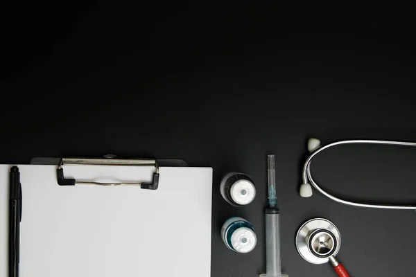 Doctor 's Day ve Covid-19 konsepti. Üzerinde mavi beyaz ilaç şişesi, iğne ve steteskop olan klip tahtası.