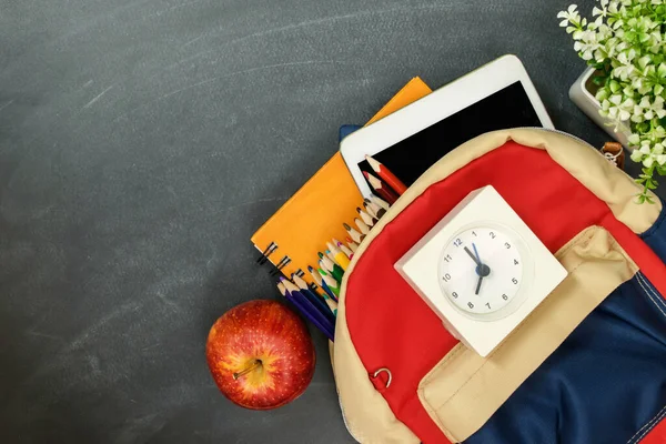 Okul konseptine geri dönelim. Okul malzemeleriyle dolu sırt çantası, saat, tablet ve elmayla tebeşir tahtası. Üst Manzara. Boşluğu kopyala