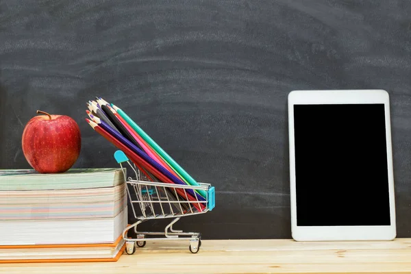 Kırmızı elma kitabın üzerinde duruyor. Kalem, tablet. Arka planda kara tahta var..