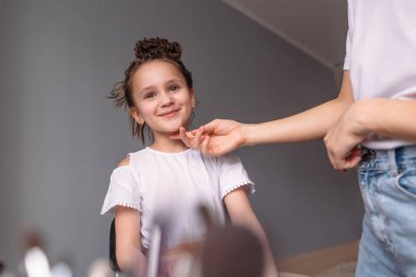 Genç anne kızına makyaj yapıyor, sabah, pencereden gelen ışık, neşeli kız çok konuşuyor.