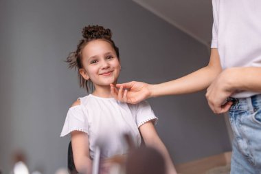 Genç anne kızına makyaj yapıyor, sabah, pencereden gelen ışık, neşeli kız çok konuşuyor.