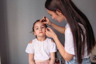 Genç anne kızına makyaj yapıyor, sabah, pencereden gelen ışık, neşeli kız çok konuşuyor.