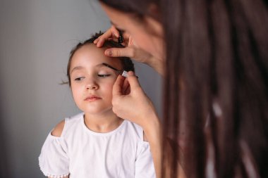 Genç anne kızına makyaj yapıyor, sabah, pencereden gelen ışık, neşeli kız çok konuşuyor.