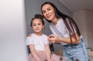 Genç anne kızına makyaj yapıyor, sabah, pencereden gelen ışık, neşeli kız çok konuşuyor.