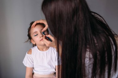 Genç anne kızına makyaj yapıyor, sabah, pencereden gelen ışık, neşeli kız çok konuşuyor.