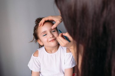 Genç anne kızına makyaj yapıyor, sabah, pencereden gelen ışık, neşeli kız çok konuşuyor.