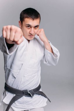 Beyaz arka planda beyaz kimono giyen genç ve güçlü bir adam yumruk atıyor.