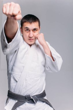 Beyaz arka planda beyaz kimono giyen genç ve güçlü bir adam yumruk atıyor.