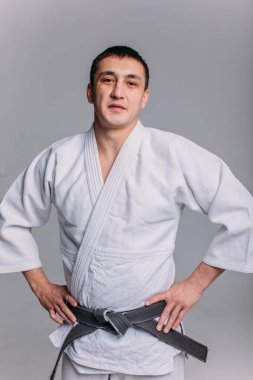 Beyaz arka planda beyaz kimono giyen genç ve güçlü bir adam yumruk atıyor.